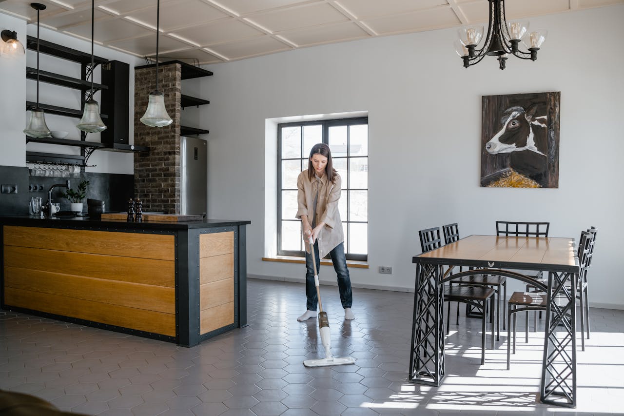 Woman mopping the floor in a contemporary kitchen and dining area with natural light.