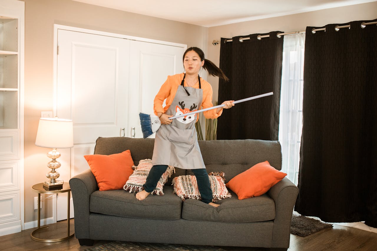 A joyful woman dances with a broom while cleaning her cozy living room.